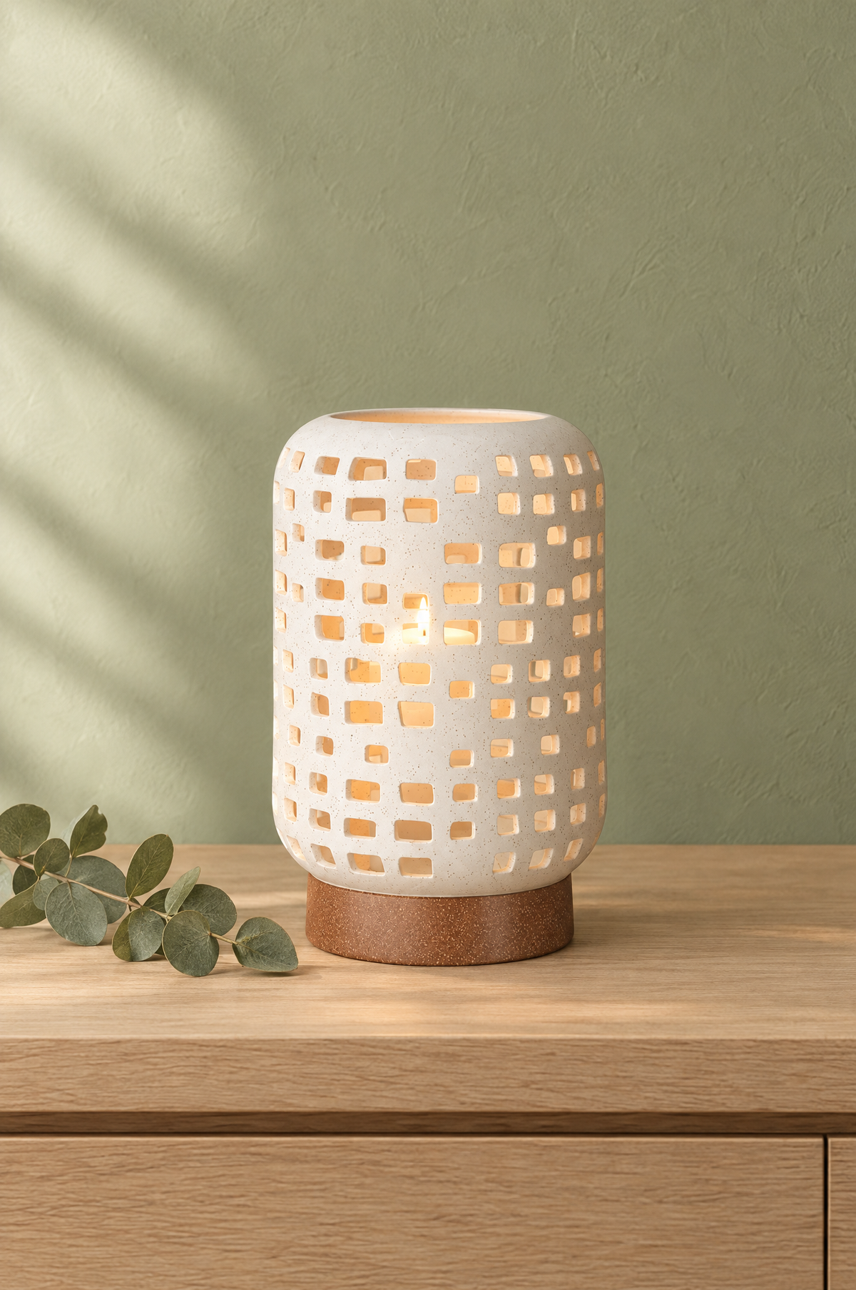 White ceramic lantern candle holder glowing on an oak console against a sage green wall